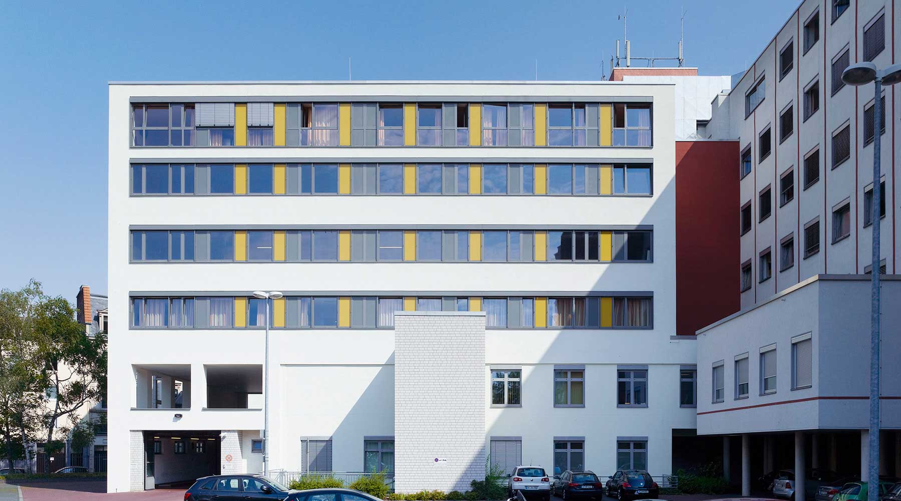 Krankenhausfassade: weiß mit Fensterreihen und gelben Akzenten