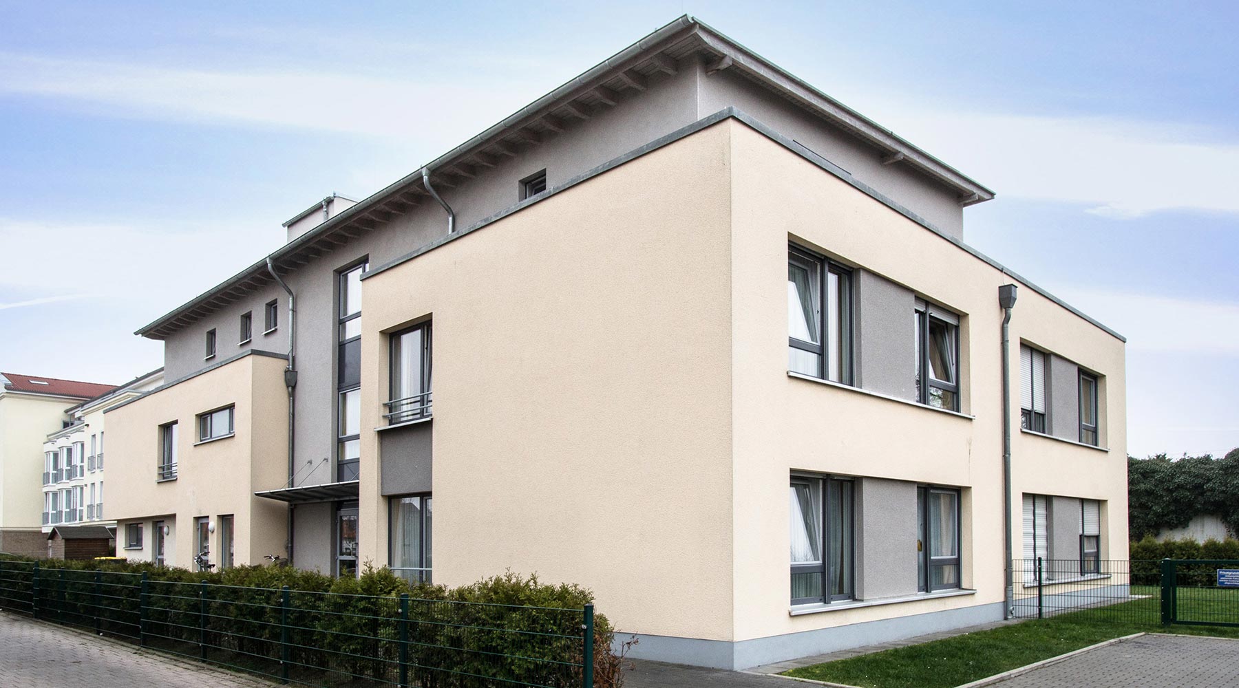 Haus Markus in Krefeld. Seitenansicht gelbe Fassade mit großen Fenstern und grauen Elementen. Staffelgeschoss in Grau.