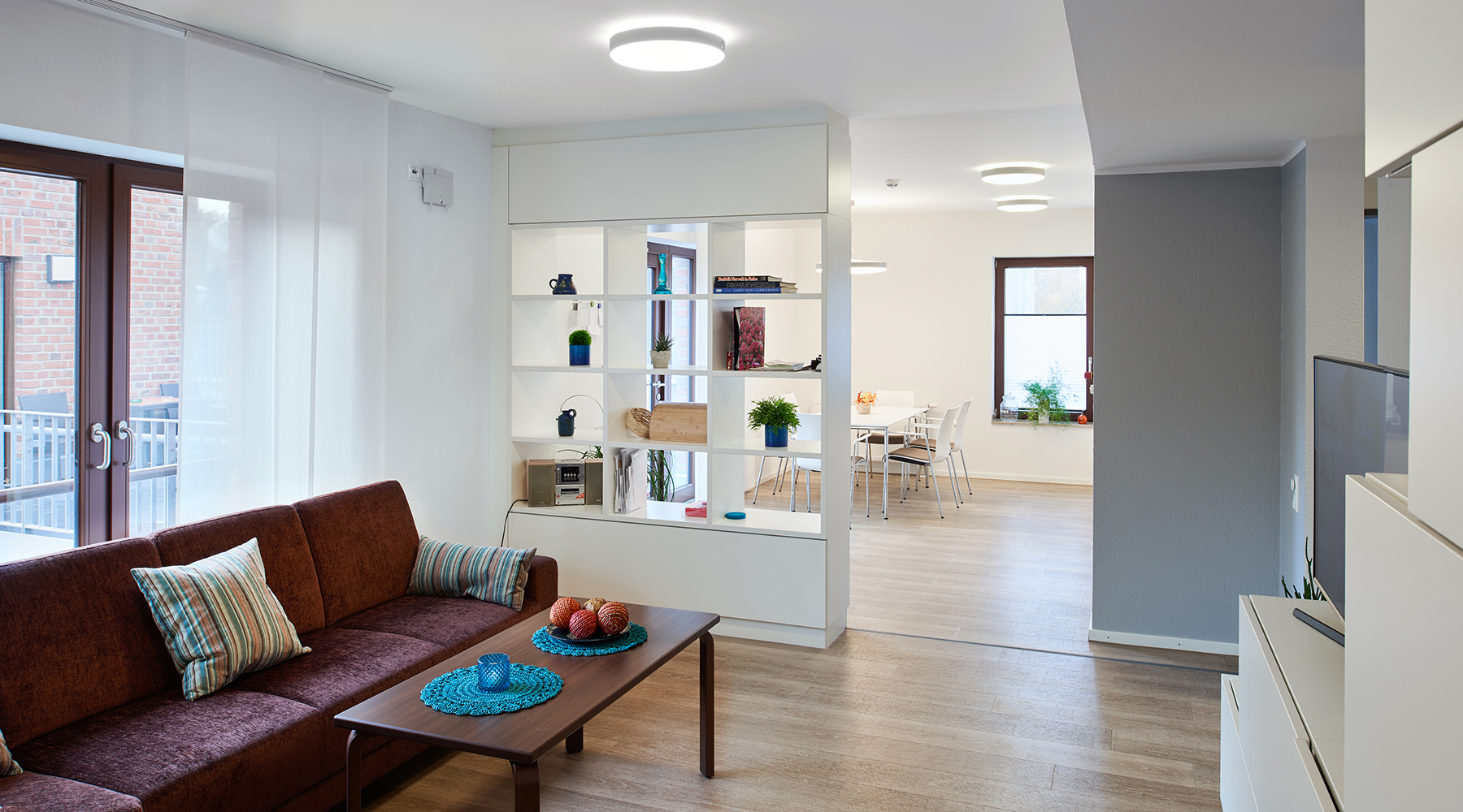 Moderner, offener Wohnbereich mit hellen Möbeln, aber dunkler Couchgarnitur.