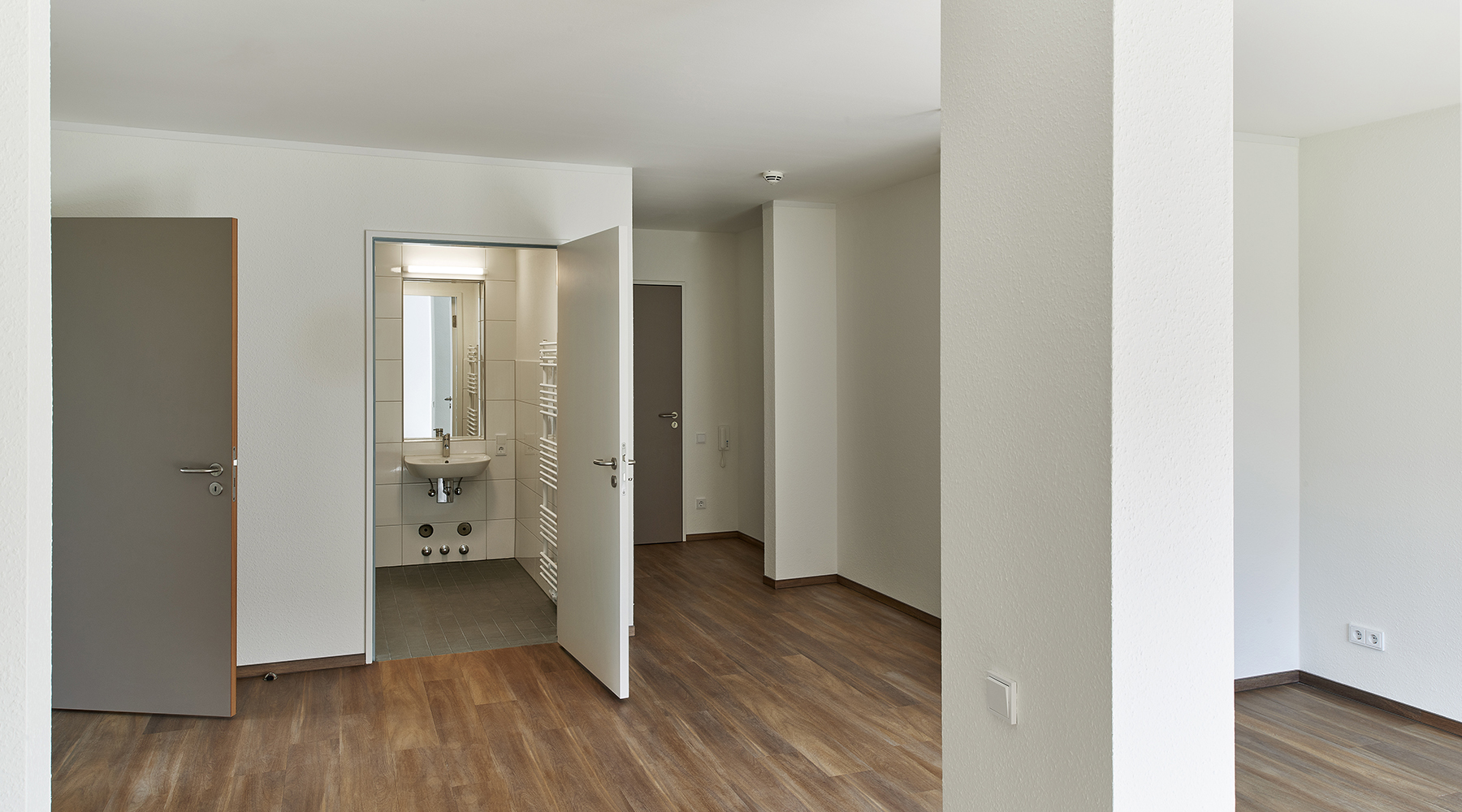 Leeres Zimmer mit Holzboden und weißen Wänden und einem kleinen Badezimmer.
