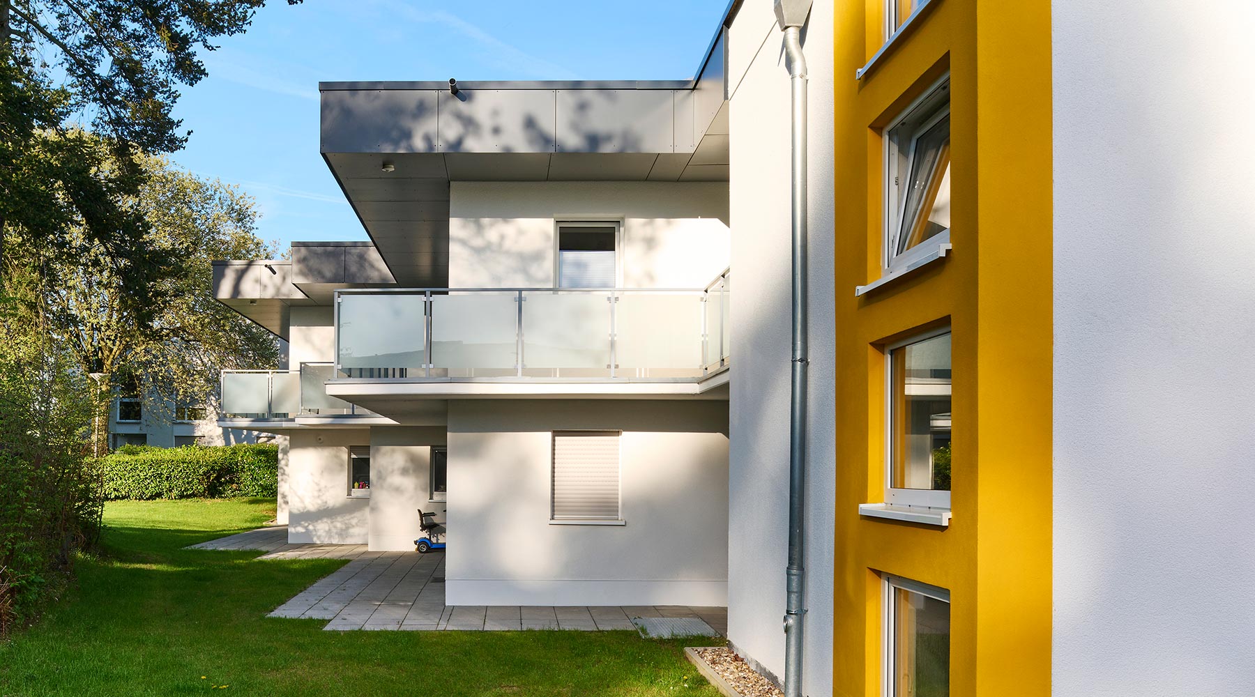 Wohnanlage am Reulert in Aachen. Seitenansicht des Wohnkomplexes, links: Flachdachhäuser weiß, mit gelbem Farbakzent.